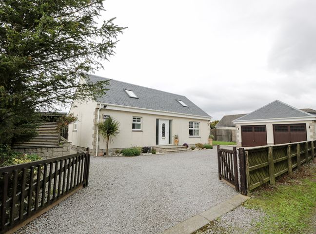 A detached house with gravel driveway and double garage next to a wooden fence at The Bothy in Southerness