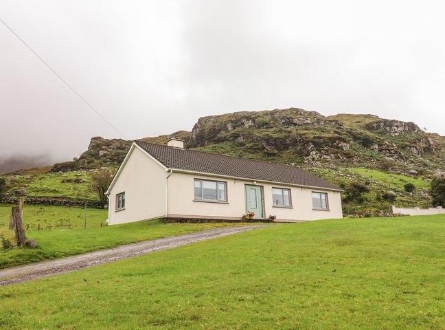 A single story house with a green door on a grassy hill with rocky hills in the background at Lyreboy in Glencar County Kerry
