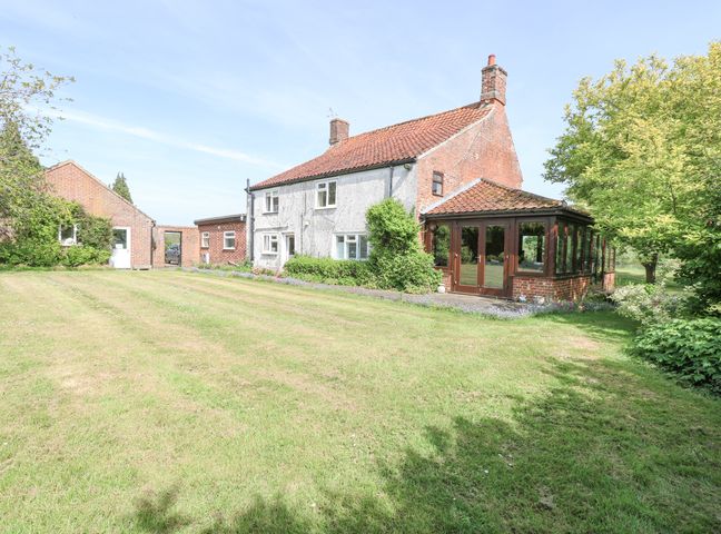 A brick and white house with a conservatory and an adjoining building on a lawn at Lyons Green in Little Fransham near Swaffham