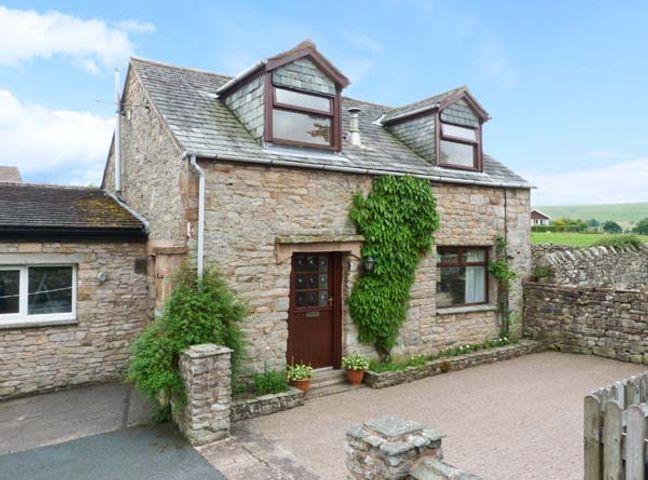 A stone house with two dormer windows green climbing plants and a courtyard at Mews Cottage in Pooley Bridge near Penrith