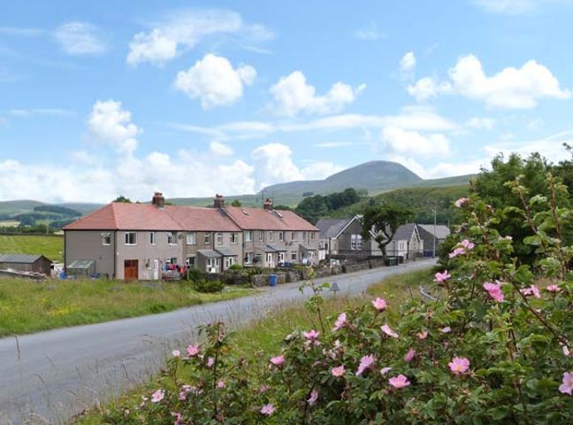 A row of houses along a road with flowers and greenery in the foreground and hills in the background at 4 Helwith Bridge Cottages Helwith Bridge near Horton-in-Ribblesdale