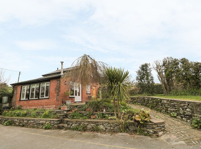 A brick house with multiple windows and a small garden with plants and a paved pathway at Beck Cottage in Pennington near Ulverston