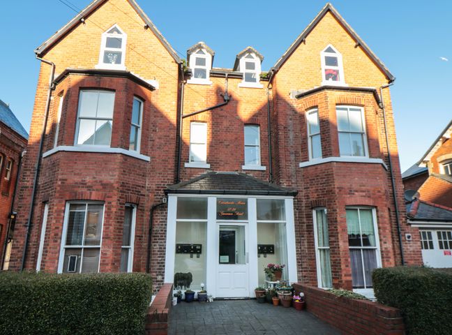 A brick apartment building with a central white door and multiple windows surrounded by plants at Carisbrooke House Apartment 6 Scarborough