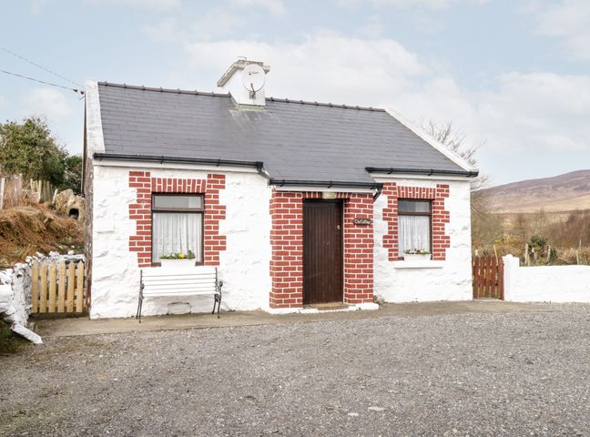 A small cottage with white walls and red brick around windows and door with a bench outside at The Cottage in Newport County Mayo