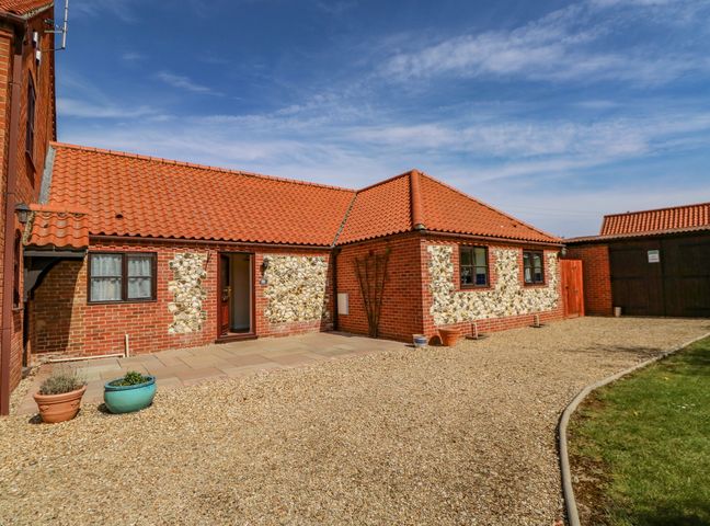 A brick and stone house with a red tiled roof and a gravel driveway at The Granary Cottage in Gayton near King's Lynn