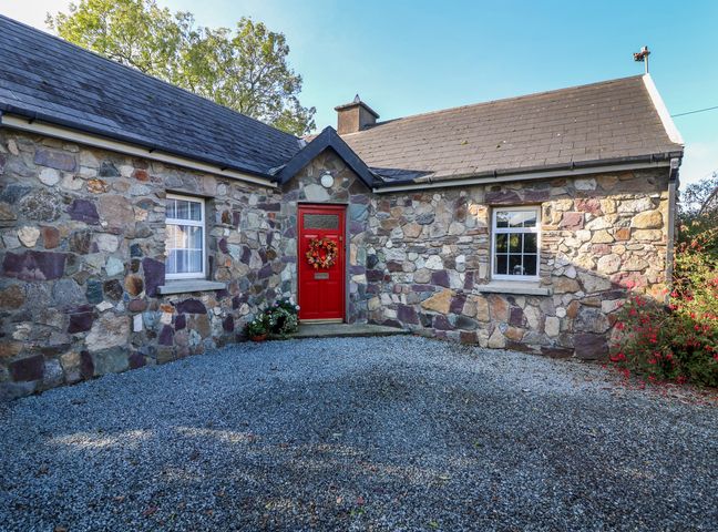 Stone cottage with a red door and two windows on a gravel driveway at Rose Cottage in Duncannon County Wexford