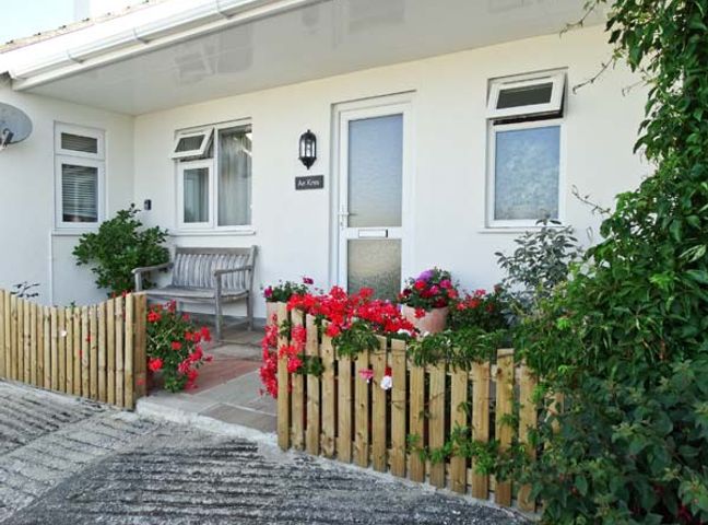 The entrance of a white house with a wooden bench a wooden fence and red flowers at An Kres in Mevagissey