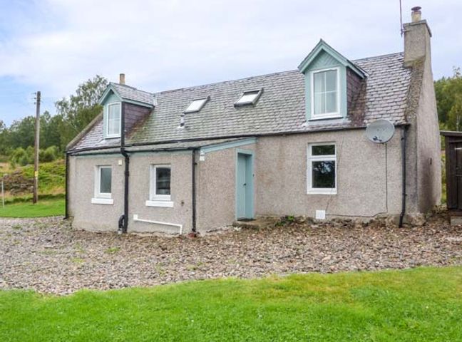 A stone house with a tiled roof and blue framed windows surrounded by grass at Easter Duthil Cottage in Carrbridge