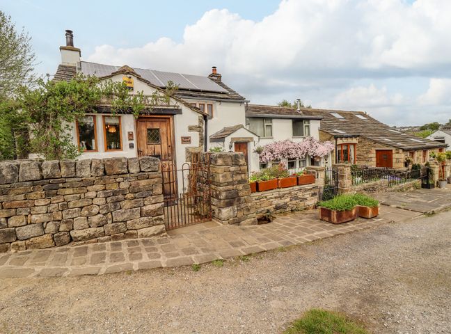 A stone and white cottage with wooden doors and flower planters along the stone wall at The Dairy in Haworth