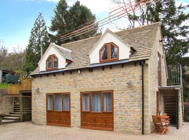 A stone house with wooden framed windows and a small outdoor seating area at Rowan Studio Cranham near Gloucester