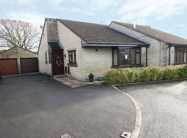 A stone semi detached house with a tiled roof a driveway two garages and bushes at 14 Silverlands Close in Buxton