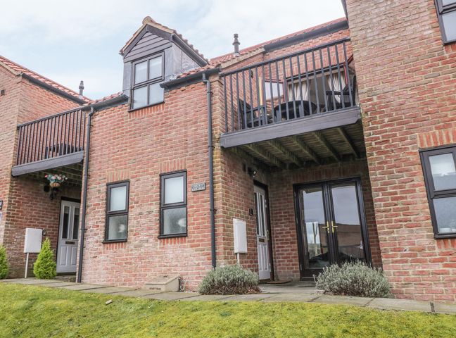 Exterior view of a brick townhouse with white doors balconies and a grass lawn at Cricket Cottage in Whitby