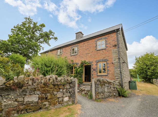 A brick and stone house with wooden framed windows and a stone wall in front at Byrdir Cottage in Rhayader