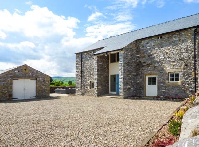 A courtyard with gravel in front of two stone buildings under a blue sky at Ox Hey Barn in Sawley near Bolton-by-Bowland