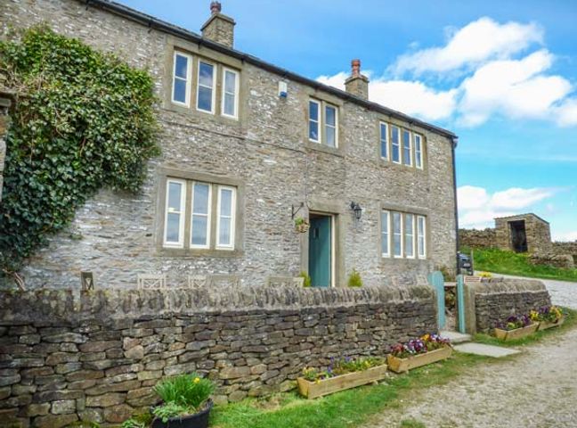 A stone house with multiple windows and a small stone wall with flower planters at Street Head Farm Lothersdale near Skipton