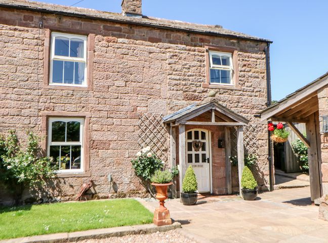 Stone house exterior with white door and windows small garden and plants near entrance at The Cow Byre in Barras near Kirkby Stephen