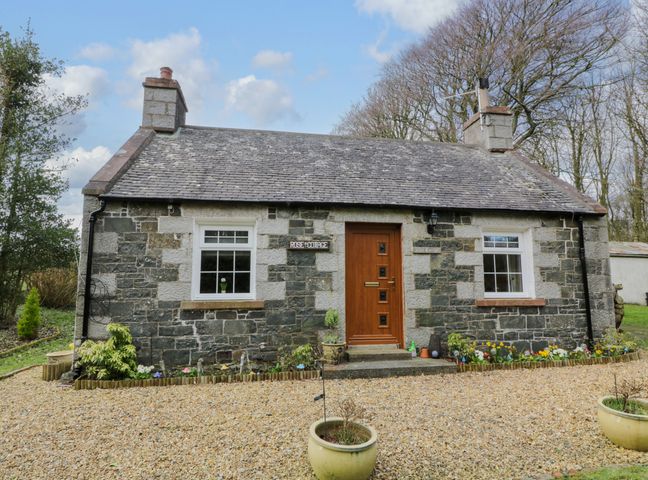 A stone cottage with two windows a wooden door and flower beds with gravel in front at Rose Cottage in Stranraer