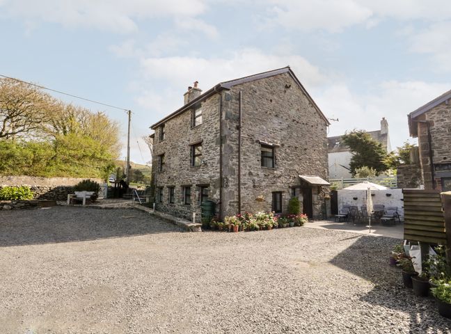 A stone house with multiple windows a gravel driveway and potted plants at Raceside Cottage Kirksanton near Millom