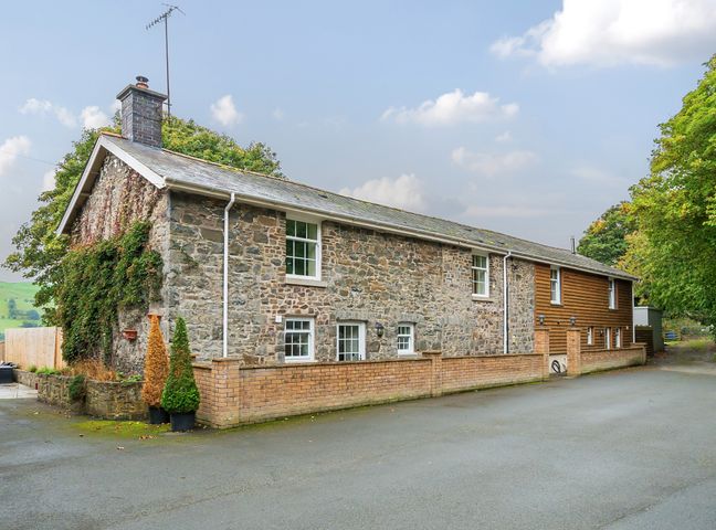 A stone and wood exterior of a long house with windows and a brick wall at Old Rectory Cottages Aberhafesp near Newtown