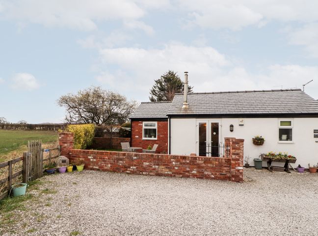 A small house with a gravel driveway a brick wall outdoor chairs and potted plants at The Old Stable in Mold