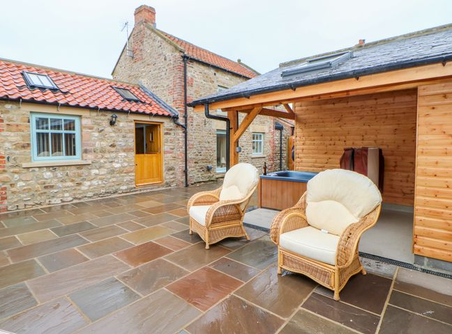 An outdoor patio area with two cushioned wicker chairs stone walls and a wooden building at The Dove Cote in Brompton-on-Swale