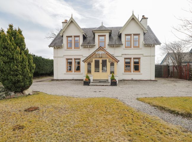 A two-story house with multiple windows and a central entrance surrounded by a gravel driveway and lawn at Glencanisp in Aviemore