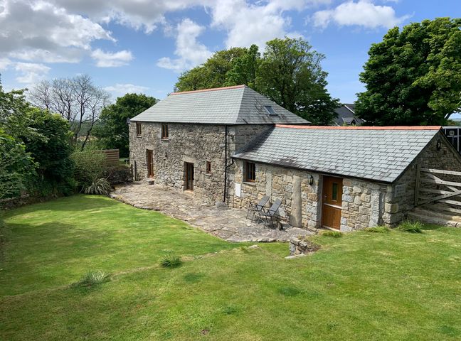 A stone house with slate roof and two chairs outside on a stone patio surrounded by grass and trees at Sleepy Fox in Blisland