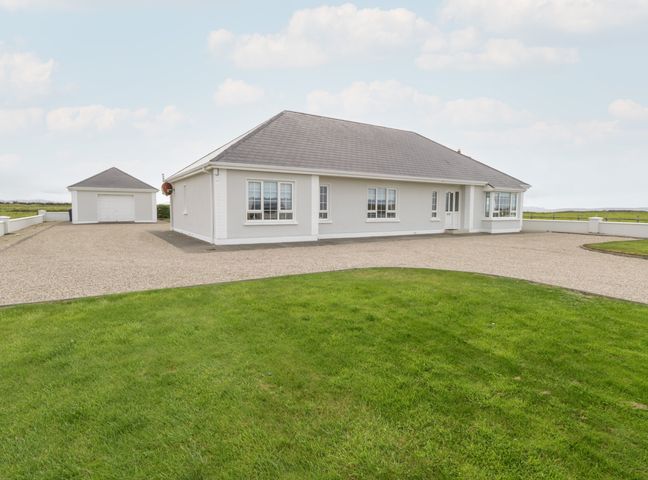 A single-story house with a detached garage and a gravel driveway surrounded by green grass at Shraigh Beach in Belmullet County Mayo