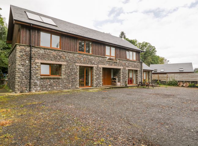 Stone and wood house with multiple windows and a gravel driveway at Woodland Villa in Oban