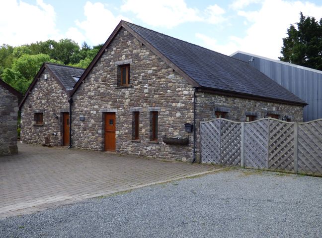 A stone barn with multiple wooden doors and windows next to a wooden fence at Riverside Barn in Gilwern near Crickhowell and Abergavenny