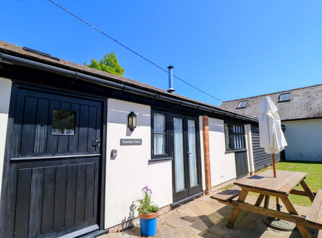 Exterior view of a building with black doors and windows a wooden picnic table and umbrella on a patio at Rowdens Barn in Winterborne Stickland