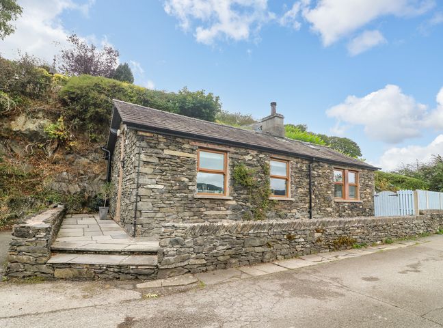 A stone cottage with three windows and a stone wall along the road at The Lodge in Bouth near Newby Bridge