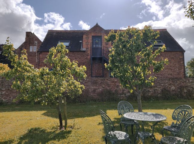 A garden with trees and metal table and chairs in front of a stone house at The Coach House in North Newton near Bridgwater