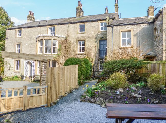 A garden area with gravel paths and flower beds in front of a stone house at Whitefriars Lodge in Settle