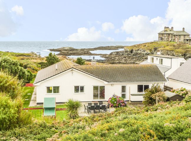 A white house with a patio and outdoor dining furniture near rocky coastline at The Beach House Trearddur Bay in Trearddur Bay
