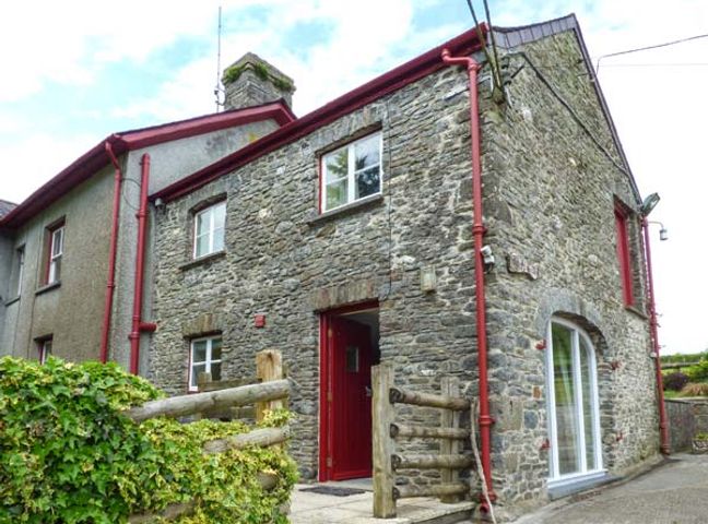 A stone house with red pipes and a wooden fence at Crud-y-Barcud in Pumsaint near Lampeter