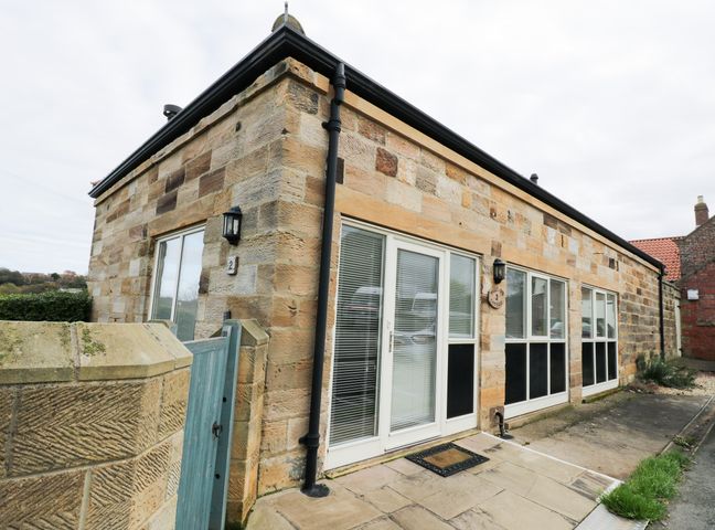 A stone cottage with white framed windows and doors next to a small blue gate and a stone wall at Mallard Cottage in Whitby