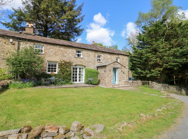 A stone house with a grassy yard and patio furniture surrounded by trees at Farriers Cottage Garsdale