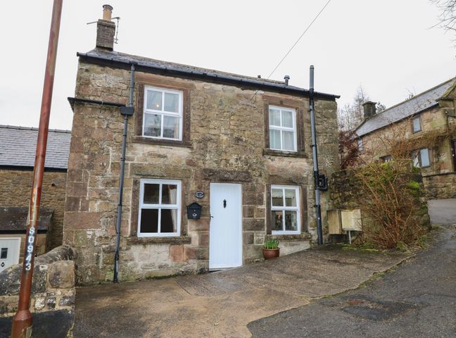 A stone cottage with white framed windows, a white door, a mailbox, and a potted plant at Walton Cottage in Winster