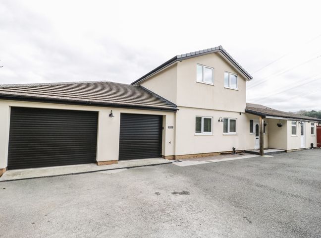 The exterior of a two story house with two black garage doors and a driveway at Bryn Derw Holiday Cottage in Eglwysbach near Llanrwst and Conwy