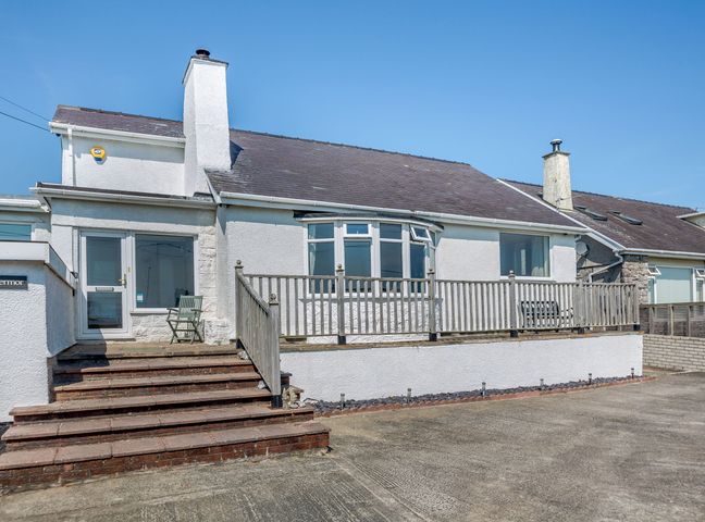 The exterior front view of a white house with stairs leading to a porch and wooden railing at Abermor in Moelfre
