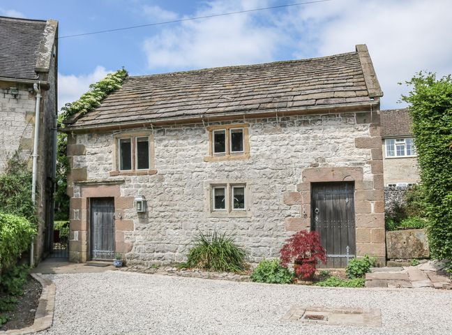 A stone building with two wooden doors and four small windows surrounded by plants at The Studio in Parwich near Ashbourne