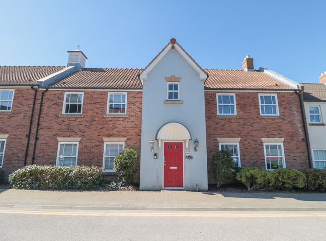 A brick townhouse with a red front door and small bushes along the front at Sunny Bay in The Bay near Filey
