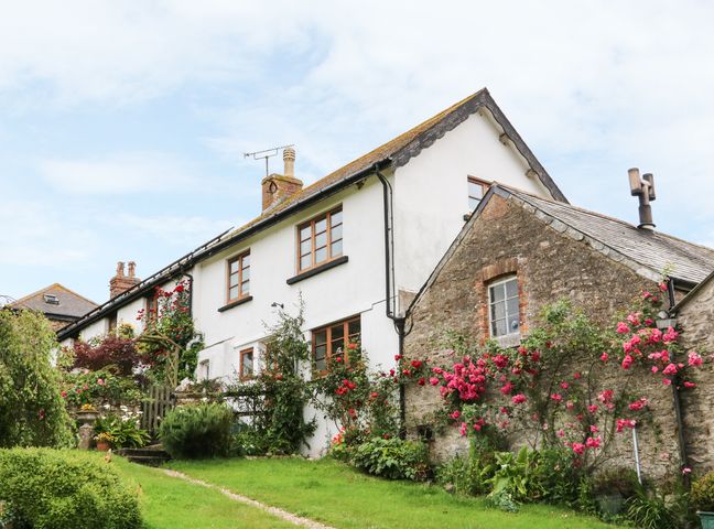 A white and stone house with wooden windows and a garden with pink and red flowers at Toms House in Berrynarbor near Combe Martin