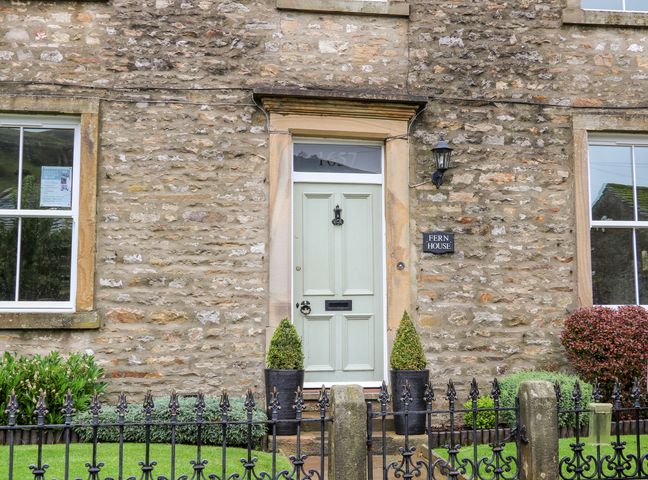 Stone house exterior with a light green front door two potted plants and metal fence at Fern House in Kettlewell