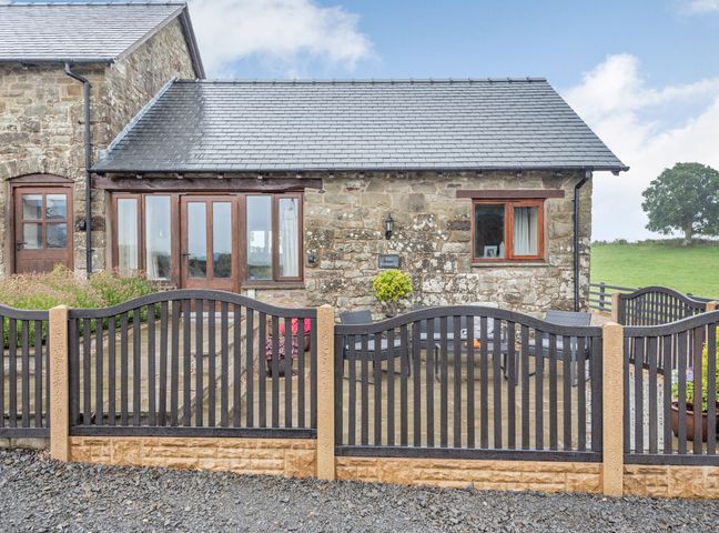 A stone building with a slate roof behind a black metal fence at The Granary in Llanfair Caereinion near Welshpool