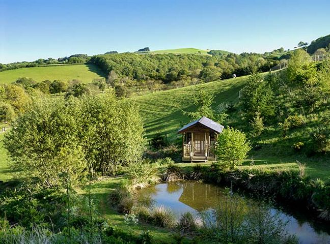 A small wooden cabin near a pond with trees and hills in the background at Black Mountain View in Llanafan Fawr near Builth Wells
