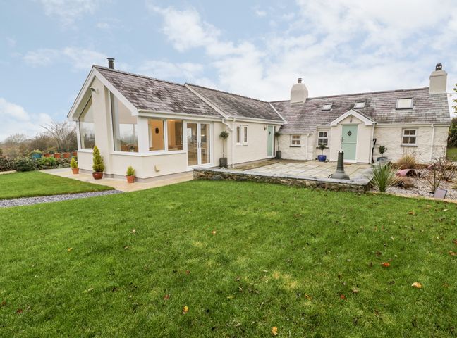 A house with a grass lawn and a stone patio with plants at Ty'n Lon Bach in Llandwrog
