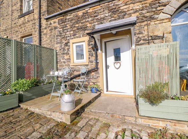 A stone exterior with a white door, small window, metal table and chairs, planters, and a fenced area at The Mistle Carr Farm in Ripponden