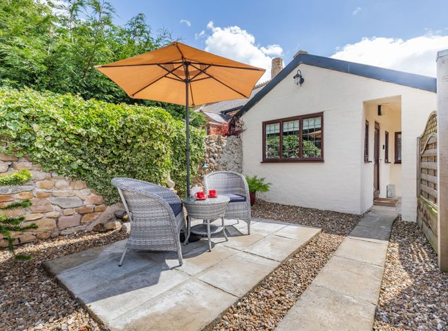 A small outdoor patio with two wicker chairs a round table and an umbrella next to a white brick building at Willow Cottage in Ulrome near Skipsea